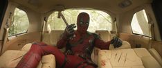 a deadpool is sitting in the back seat of a car and holding a knife