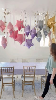 a woman standing in front of a table with chairs and balloons hanging from the ceiling