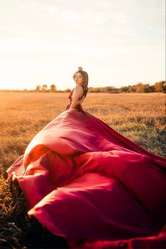 a woman in a red dress sitting on top of a grass covered field at sunset