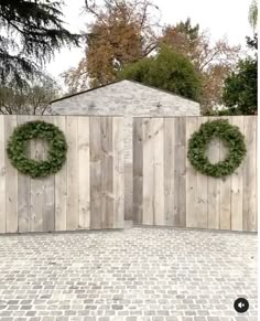 a brick driveway with a wooden gate and wreath on the wall, surrounded by trees