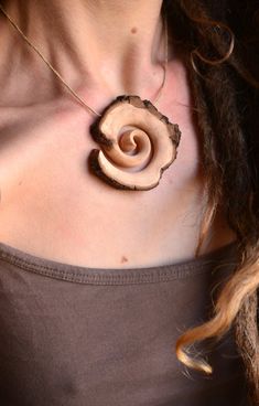 a woman wearing a brown shirt with a wooden necklace on her neck and an earring in the shape of a spiral