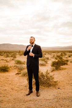 a man in a suit and tie standing in the middle of an empty desert field