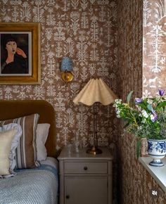 a bed room with a neatly made bed next to a night stand and flowers on the nightstand