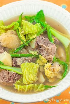 a white bowl filled with meat and veggies on top of a colorful table cloth