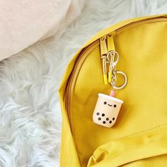 a yellow backpack with a keychain hanging from it's side and a coffee cup on the front pocket