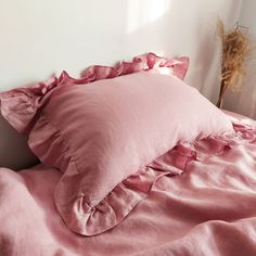 a pink comforter with ruffled edges and pillows on a bed in a bedroom