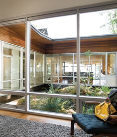 a person sitting on a bench in front of a glass wall looking out onto the yard