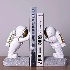 two booksends made to look like astronauts in white suits, one holding the other's hand