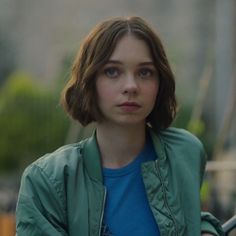 a woman in a blue shirt and green jacket is looking at the camera with an intense look on her face