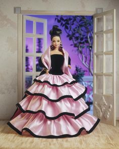 a barbie doll dressed in a pink and black ball gown standing on a wooden floor