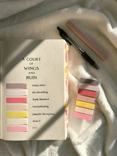 a court of wings and ruin book next to a pen on a white blanket with other items