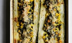 two corn on the cob with cheese and herbs in a baking dish, ready to be cooked