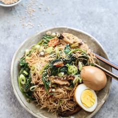 a bowl filled with noodles and vegetables next to chopsticks on top of a table