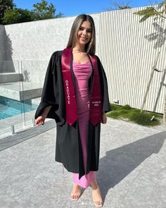 a woman standing in front of a pool wearing a graduation gown