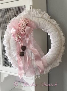 a white wreath with pink flowers and ribbons