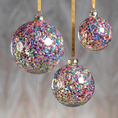 three christmas ornaments hanging from strings with colored confetti on them