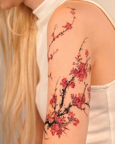 a woman's arm with red flowers on it and a bird perched on the branch