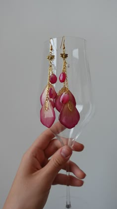 a person holding up a wine glass with some pink flowers on the bottom and gold chains hanging from it