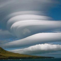 some very pretty clouds in the sky over water and land with a mountain behind it