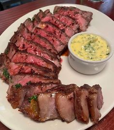 a white plate topped with meat next to a bowl of sauce