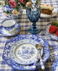 a table set with blue and white plates, silverware and strawberries on it