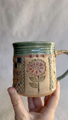 a hand holding a coffee mug with a flower painted on the outside and inside it