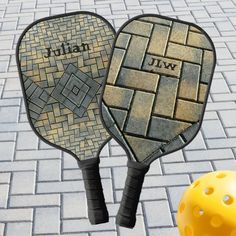 two paddles with names on them sitting next to a yellow ball and brick floor