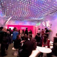 a group of people sitting at tables in a room with lights on the ceiling above them