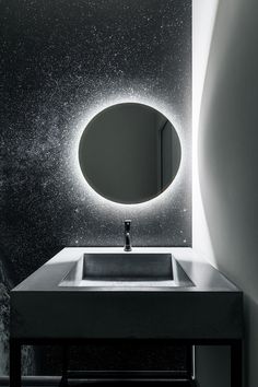 a bathroom sink under a round mirror with lights on it's sides and a black counter top