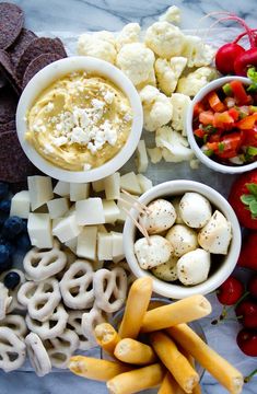 an assortment of food including crackers, vegetables and dip is displayed on a marble surface