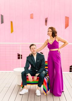 a man and woman sitting on a bench in front of a pink wall with geometric shapes