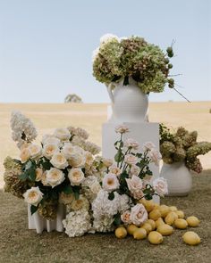 an arrangement of flowers and lemons in front of a white vase on the grass