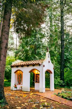 a small white building sitting in the middle of a forest