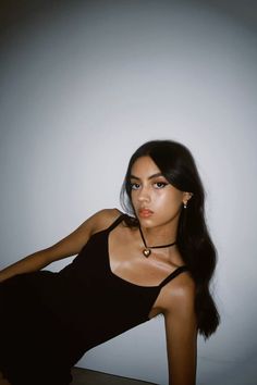 a woman in a black dress posing with her hand on her hip and looking at the camera