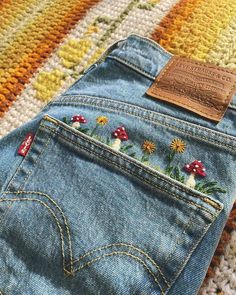 a pair of jeans with embroidered flowers on them sitting on a colorful rug next to a stuffed animal