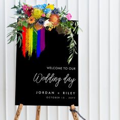 the welcome sign is decorated with colorful flowers and greenery on an easel stand