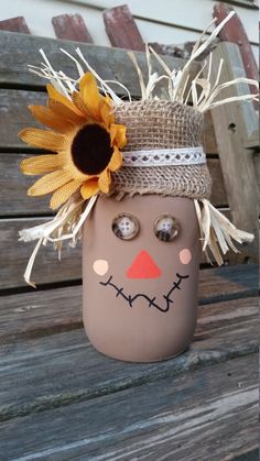 a mason jar with a scarecrow face and sunflowers on the top is sitting on a wooden bench