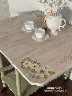 a table painted with flowers on it and two cups sitting on top of the table