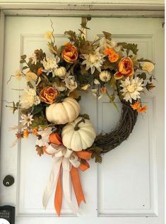 a wreath with flowers and pumpkins hanging on a door