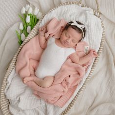 a baby is sleeping in a basket with flowers on the floor next to it and wearing a pink sweater