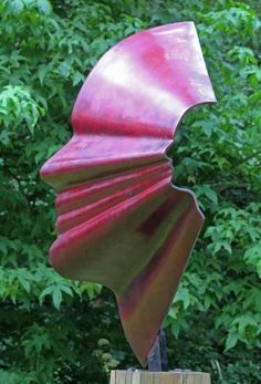 a large red sculpture sitting on top of a wooden post in front of some trees