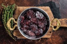 a metal bowl filled with raisins on top of a wooden cutting board next to a sprig of rosemary