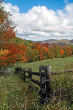 a wooden fence in the middle of a field surrounded by trees with fall foliages