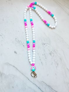 a white beaded necklace with pink, blue and green beads on a marble surface