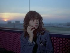 a woman sitting on a bench in front of a window with the sun setting behind her