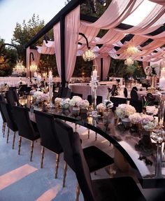 a long table with black chairs is set up for an outdoor wedding reception in the evening