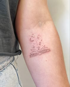 a woman's arm with a tattoo on it that has a book and stars coming out of it