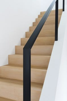 there is a black handrail on the stairs next to some white walls and wood steps