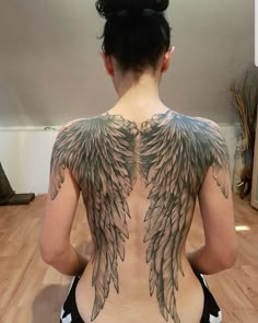 a woman sitting on the floor with her back to the camera and wings tattooed on her body