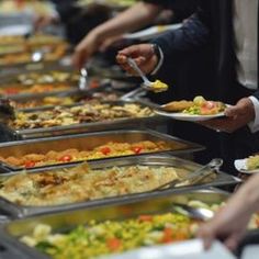 many people are serving themselves food from trays